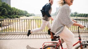 Happy couple crossing a bridge with bicycle and by foot